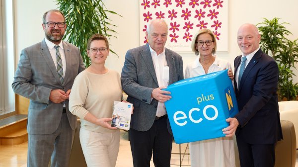 6 Personen stehen in einem Büro und halten einen blauen Würfel