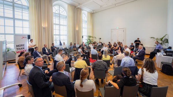 Viele Menschen sitzen in einem großen Stuhlkreis in einem hellen Veranstaltungssaal mit hohen Fenstern.