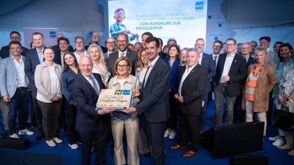 Mehrere Personen stehen auf einer Bühne und präsentieren gemeinsam einen Kuchen mit der Aufschrift "25 Jahre CCK Wirtschaftspark Kottingbrunn". Im Hintergrund ist eine große Veranstaltungswand mit Projektion zu sehen.