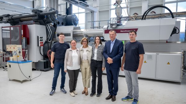 Fünf Personen stehen in einer Industriehalle vor einer großen Produktionsmaschine.