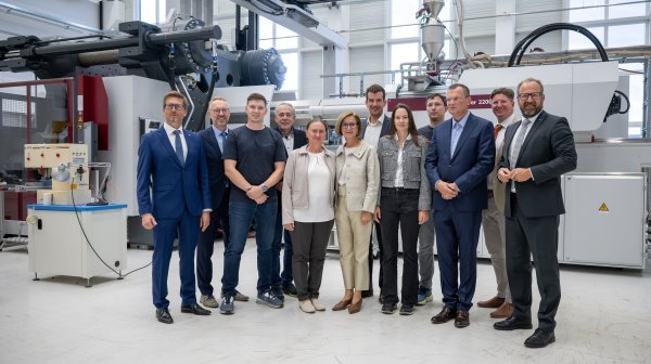 Mehrere Personen stehen zwischen großen Industriemaschinen und Produktionsanlagen.