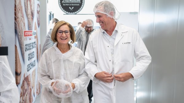 Zwei Personen in weißer Hygieneschutzkleidung gehen durch einen Betriebsbereich.