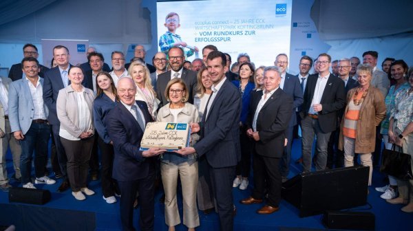 Mehrere Personen stehen auf einer Bühne und präsentieren gemeinsam einen Kuchen mit der Aufschrift "25 Jahre CCK Wirtschaftspark Kottingbrunn". Im Hintergrund ist eine große Veranstaltungswand mit Projektion zu sehen.