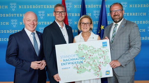 Vier Personen stehen vor einer blauen Pressewand des Landes Niederösterreich und halten gemeinsam ein großes Plakat.