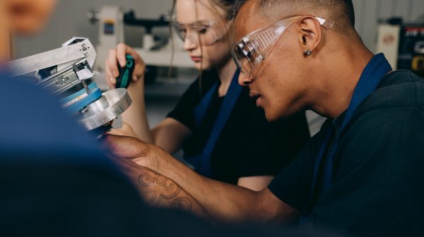 Zwei Personen mit Schutzbrillen arbeiten gemeinsam an einer technischen Maschine