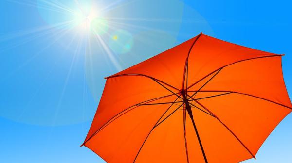 Oranger Sonnenschirm vor blauem Himmel mit Sonne