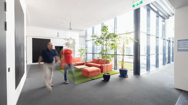 Innenansicht DGK mit oranger Sofalandschaft und 2 Personen in verschwommener  Zeitrafferansicht