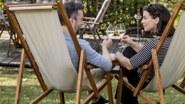 Zwei Personen im Liegestuhl stoßen mit einem Weinglas an