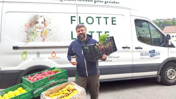 Mann mit Lebensmittelkiste steht vor kleinem Liefervan