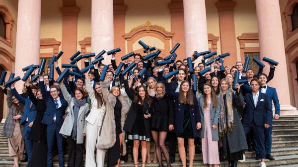 Gruppenfoto von Studierenden bei ihrem Abschluss: alle halten schwarze Rolle in ihren Händen