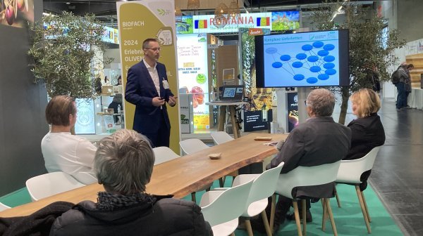 Personen sitzen an einem Tisch und hören einem Vortragenden zu