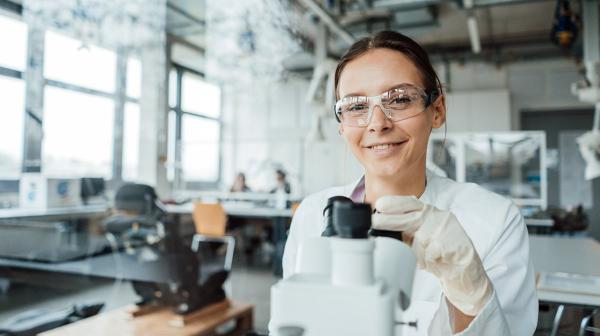 Frau mit Schutzbrille beim Mikroskopieren