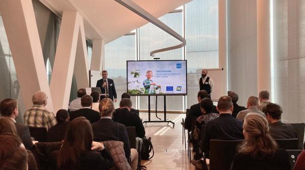 Vortragsraum mit vortragenden Personen und Publikum