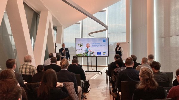 Vortragsraum mit vortragenden Personen und Publikum