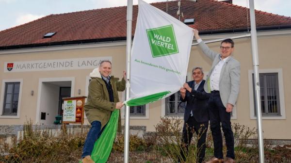 drei Männer stehen vor einem Haus und hängen eine Fahne auf 