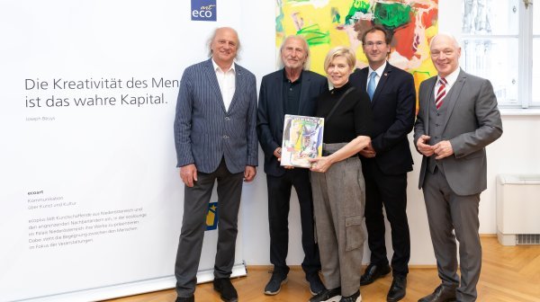 Vier Männer und eine Frau stehen vor einem Gemälde und einer Bildwand und halten einen Katalog in Händen