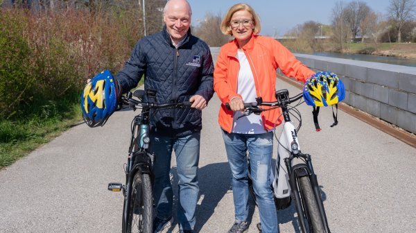 Mann und Frau mit 2 Fahrrädern und blau-gelben Helmen