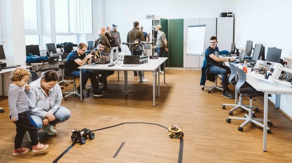 In einem Raum beschäftigen sich alle Personen mit Robotik und beweglichen kleinen Robotern