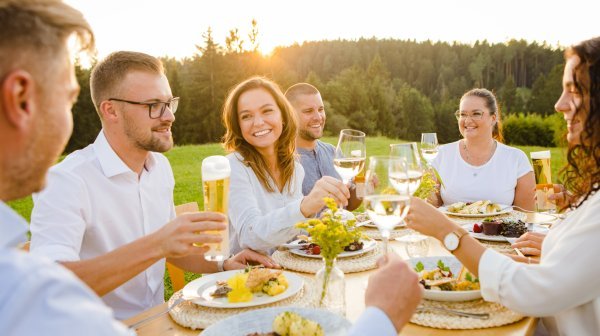 Personen sitzen draußen beim Essen und prosten sich zu