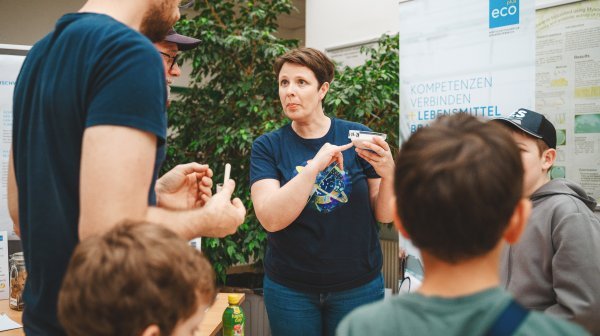 Mitarbeiterin erklärt den Besuchern etwas am Stand des Lebensmittel Cluster