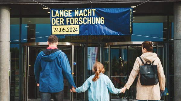 Mädchen hält Eltern an der Hand vorm Eingang zur Langen Nacht der Forschung