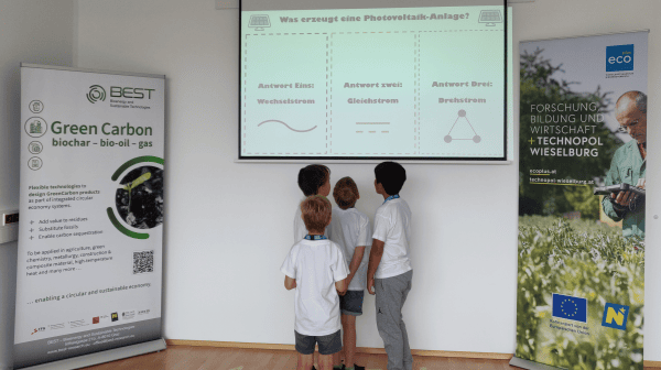 1 2 Oder3 Kinder stehen vor großem Bildschirm
