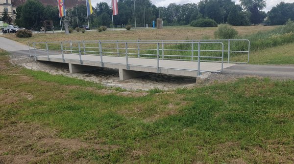 ein Radweg und eine Brücke verlaufen durch eine Wiese