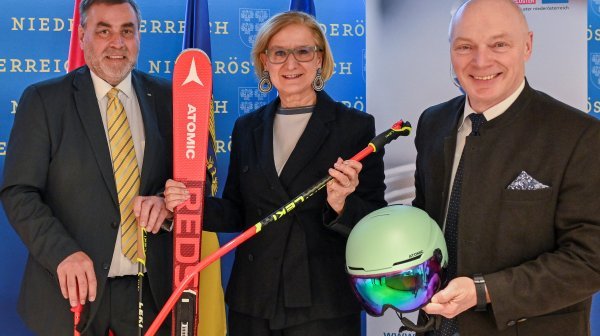 drei Personen stehen in einer Reihe und halten Ski, Helm und Stöcke 