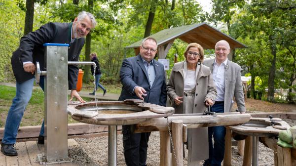 vier Personen stehen vor einem Wasserbrunnen und lachen in die Kamera