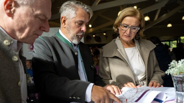 drei Personen stehen nebeneinander und schauen auf einem Plan